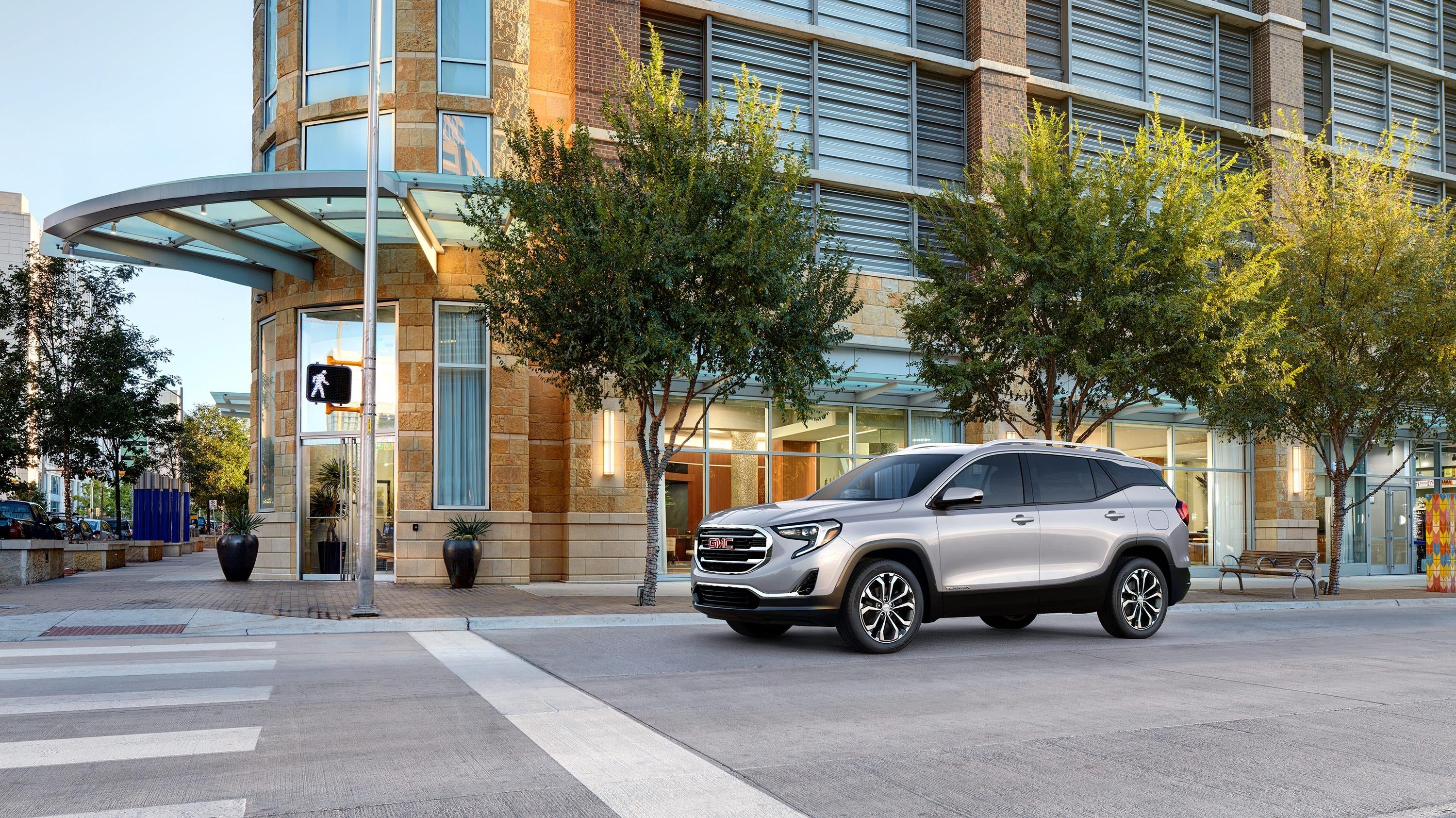 Silver GMC parked near a modern building at a crosswalk.