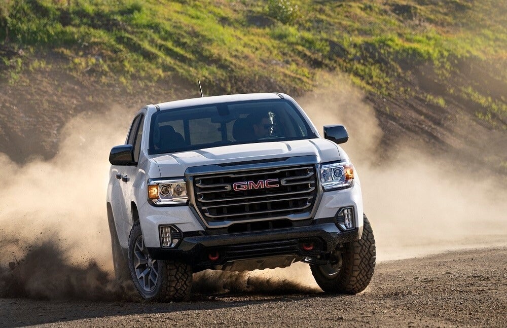 White GMC pickup truck kicking up dust on a dirt road.